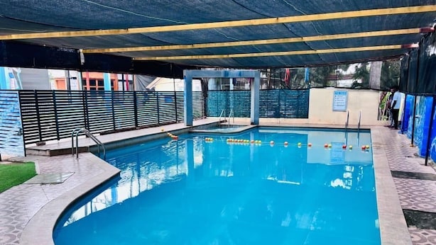 A swimming pool with a curved edge, a diving platform, and a covered area with a roof.
