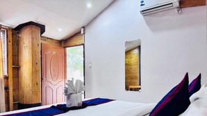 A hotel room with a bed, a wooden door, an air conditioning unit, and a small window.