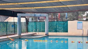 An indoor swimming pool with clear water, a diving board, and a pool rules sign on the wall.
