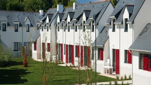 A row of white buildings with red shutters, a lawn, and trees. - Morbihan Golf Apartment for 4 (Quéven)