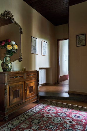 Un corridoio con un comò in legno, un vaso con fiori e un tappeto decorato.