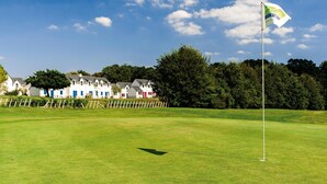 A golf course with a flag, a white fence, and houses in the background. - Brittany Golf Cottage for 4 (Quéven)