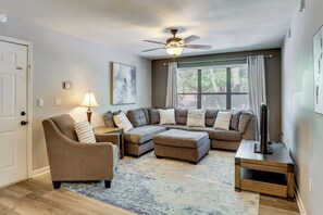 Ein Wohnzimmer mit Ecksofa, einem Sessel, einem Couchtisch, Deckenventilator und einem TV-Schrank.