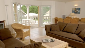 A living room with a sofa, armchairs, a coffee table, and a sliding glass door leading to an outdoor area with a white umbrella and chairs. - Villa for 6 People with Swimming Pool (Lacanau)