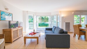 A modern living room with a sofa, coffee table, TV, and dining area with chairs and a table. - Villa for 6 People with Swimming Pool (Lacanau)