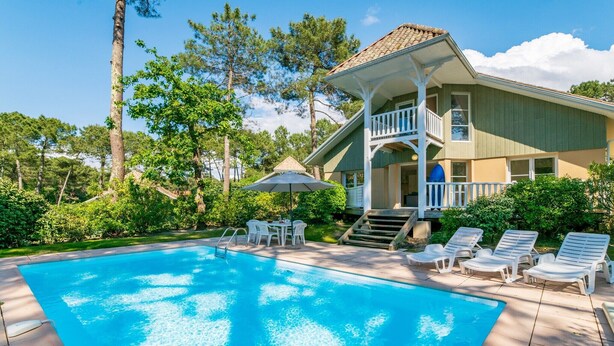 A pool with lounge chairs and a dining table, surrounded by greenery and a house with a balcony. - Villa for 6 People with Swimming Pool (Lacanau)