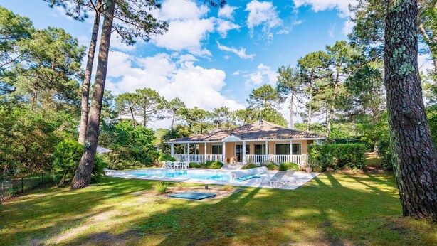Una casa con piscina, rodeada de árboles y un césped cuidado.