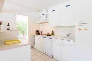 Une cuisine moderne avec des meubles blancs, un lave-vaisselle, une machine à café et une fenêtre donnant sur un espace verdoyant.