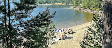 Uitzicht op een meer met een strand, bomen en een berg op de achtergrond.