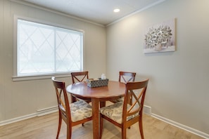 A dining area with a round wooden table, four chairs, a window with blinds, and a wall-mounted artwork.