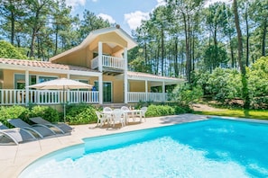 A two-story house with a pool, a balcony, and a patio with chairs and umbrellas. - Spacious Atlantic Family Villa (Lacanau-Ocean)