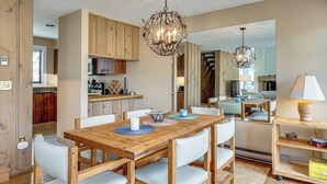 Un comedor amplio con una mesa y sillas de madera, una araña y vista a la cocina.