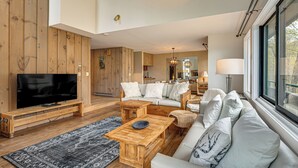 Una sala de estar moderna con un televisor de pantalla plana, muebles de madera, un sofá y un ventanal grande.