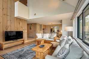 Ein modernes Wohnzimmer mit Fernseher, Holzmöbeln, einer Couch und einem großen Fenster.