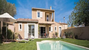 Una casa de dos pisos con piscina, mobiliario exterior y un porche cubierto.