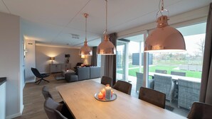 A modern dining area with a wooden table, candle centerpiece, and pendant lighting. - Modern, luxurious and very comfortable holiday home with sauna, jacuzzi, BBQ Green Egg and trampoline (Colijnsplaat)