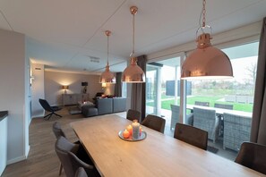 A modern dining area with a wooden table, candle centerpiece, and pendant lighting. - Modern, luxurious and very comfortable holiday home with sauna, jacuzzi, BBQ Green Egg and trampoline (Colijnsplaat)