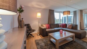 A modern living room with a sofa, a coffee table, a lamp, and a vase with flowers. - Modern, luxurious and very comfortable holiday home with sauna, jacuzzi, BBQ Green Egg and trampoline (Colijnsplaat)