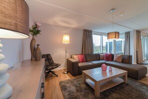 A modern living room with a sofa, a coffee table, a lamp, and a vase with flowers. - Modern, luxurious and very comfortable holiday home with sauna, jacuzzi, BBQ Green Egg and trampoline (Colijnsplaat)