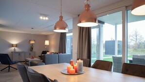 A modern living room with a dining table, sofas, and a large window. - Modern, luxurious and very comfortable holiday home with sauna, jacuzzi, BBQ Green Egg and trampoline (Colijnsplaat)