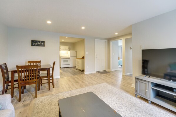 A living room with a dining table, chairs, a TV, and a kitchen in the background.
