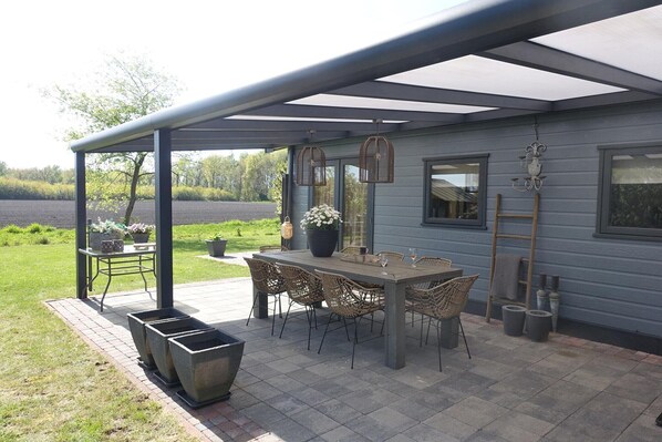A covered patio with a table and chairs, potted plants, and a view of the landscape.
