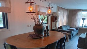 Un comedor con una mesa redonda, sillas, lámparas colgantes, un florero con ramas y un candelabro.