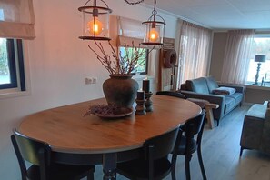 A dining area with a round table, chairs, pendant lights, a vase with branches, and a candle holder.