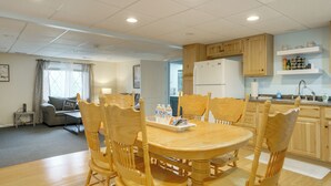 A dining area with a wooden table and chairs, a refrigerator, and a kitchen counter with shelves.