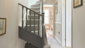 Una escalera con barandilla gris y alfombra estampada que conduce a una habitación con puerta y obras de arte enmarcadas en la pared.