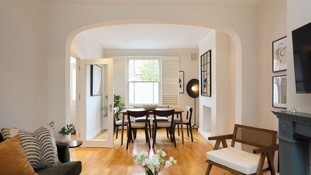 Una sala de estar con un sofá, una mesa de comedor con sillas, una chimenea y un televisor montado en la pared.