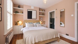 Un dormitorio con cama, mesitas de noche, un espejo, un radiador y una ventana con persianas.