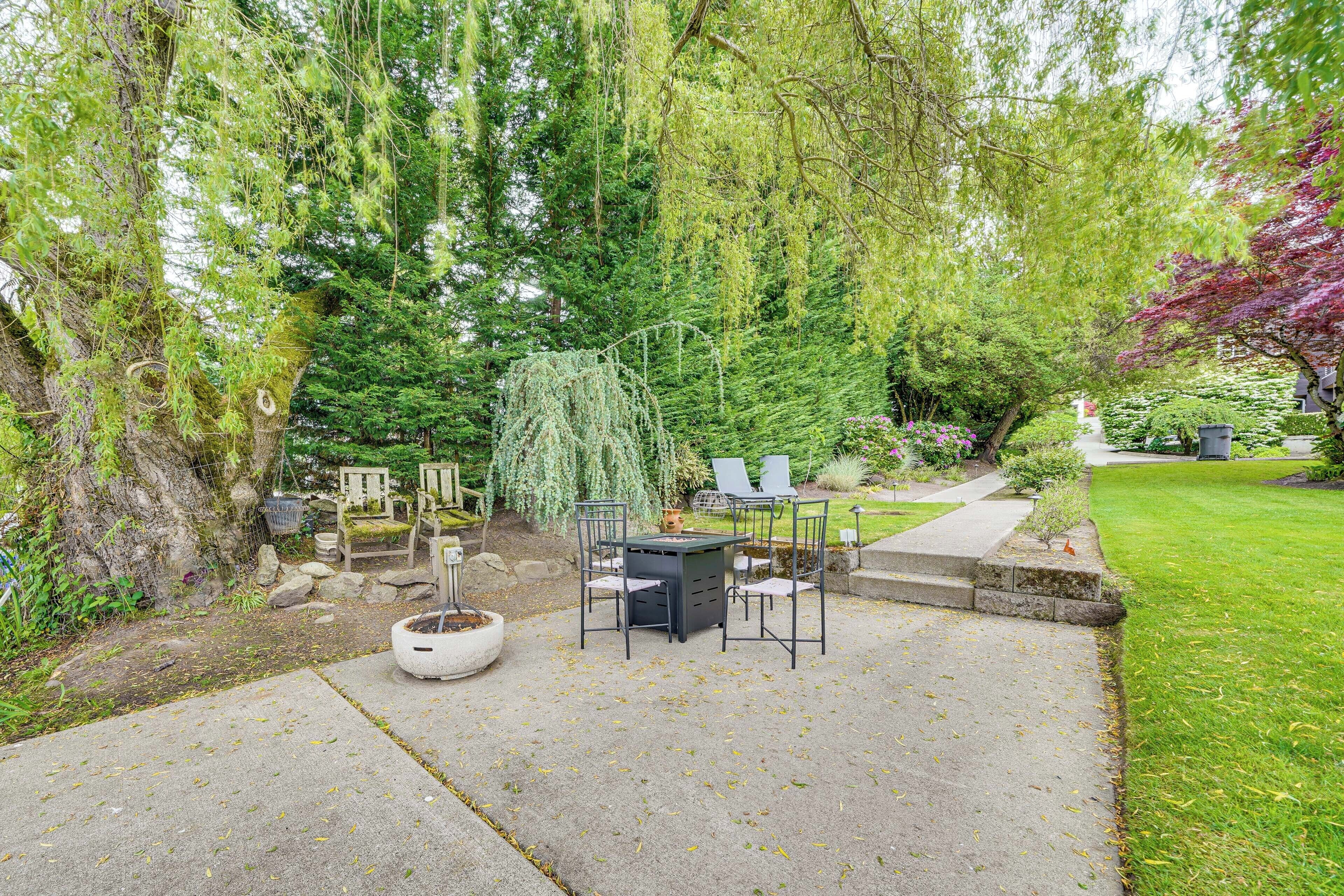 Een terras met een tafel en stoelen, omringd door bomen en een verzorgd gazon.