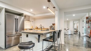 Une cuisine moderne dotée d’un réfrigérateur en acier inoxydable, d’un îlot central avec des tabourets de bar et d’un design épuré et minimaliste.