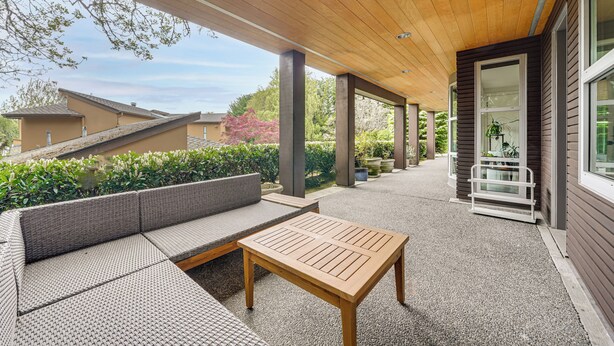 Un espace extérieur aménagé, abrité, avec une table en bois et un canapé en osier.