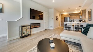 Un salon moderne avec une cheminée, un canapé, une table basse et un coin cuisine à l’arrière-plan.