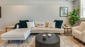 Un salon moderne avec un canapé d’angle, une table basse ronde et une grande plante.