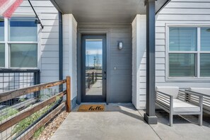 A front porch with a door, a bench, a 'hello' mat, and a fence with plants. - Sleek, Modern Denver Area Gem in Planned Community (Westminster)