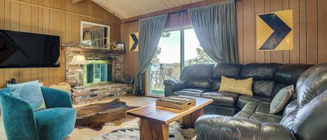 A living room with a leather sofa, teal armchair, wooden coffee table, and a TV mounted on the wall.
