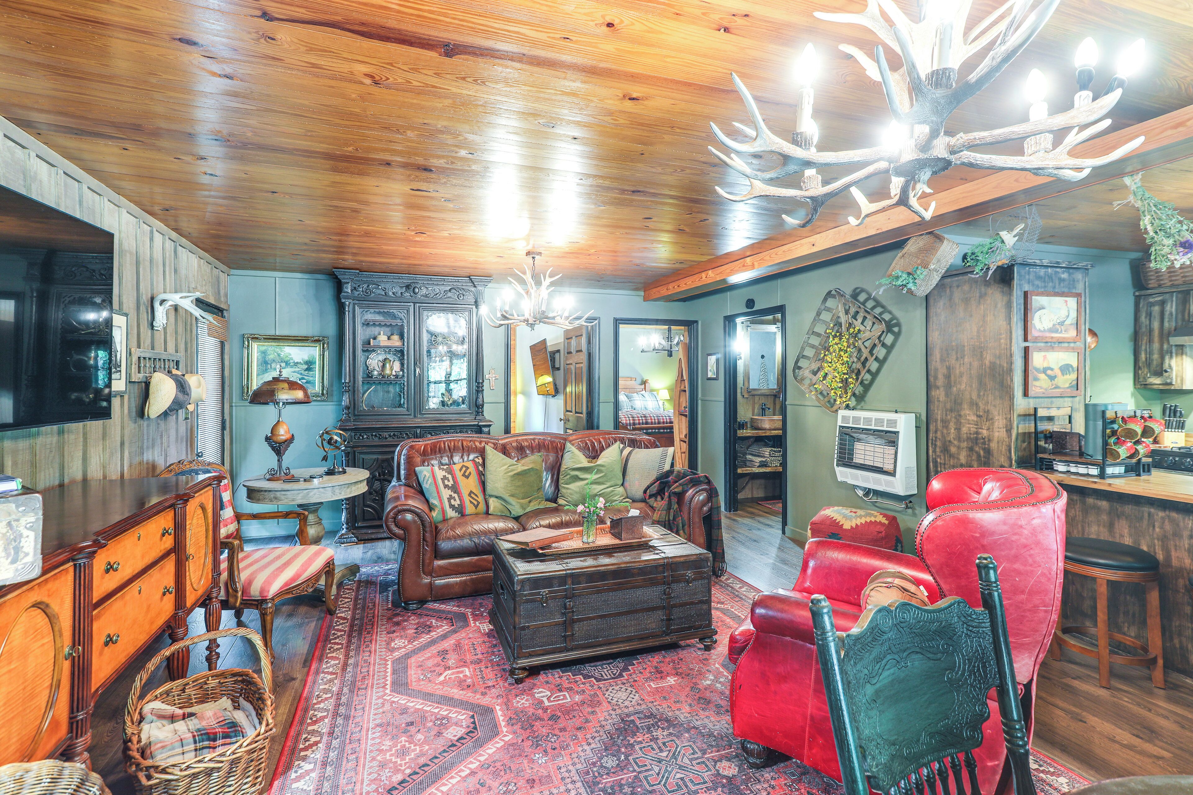 Un salon chaleureux avec un plafond en bois, un grand lustre, un canapé en cuir rouge, un fauteuil en cuir marron et une table basse de style vintage.
