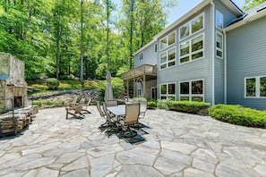 A stone patio with outdoor furniture, a stone fireplace, and a view of a two-story building with large windows. - Group-Friendly Mtn Estate 2 Mi to Dtwn Waynesville (Waynesville)