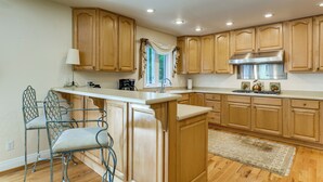 Una cocina con armarios de madera, extractor de acero inoxidable, barra y ventana con cortinas.