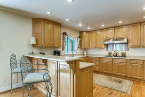 Una cocina con armarios de madera, extractor de acero inoxidable, barra y ventana con cortinas.