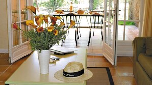 A room with a dining table set for two, a vase with flowers, a hat, and a view of the outdoors. - Large Duplex House for 10 in Fayence (Fayence)