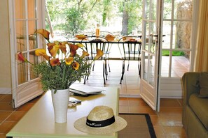 Ein Zimmer mit Esstisch für zwei Personen, einer Blumenvase, einem Hut und Blick ins Freie.