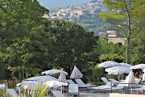Eine Terrasse mit Liegestühlen und Sonnenschirmen mit Blick auf eine Hügelstadt.