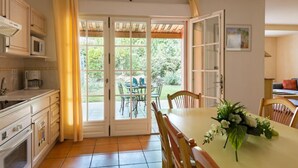 A kitchen with a dining area, a table with chairs, a flower arrangement, and a view through the glass doors. - Large Duplex House for 10 in Fayence (Fayence)