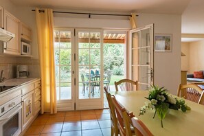Eine Küche mit Essbereich, einem Tisch mit Stühlen, einer Blumenkomposition und Blick durch Glastüren.
