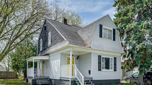A two-story house with a porch, a front door, and a staircase leading to the entrance. - Gateway to Dtwn Port Huron & Lake! Cozy Home (Port Huron)