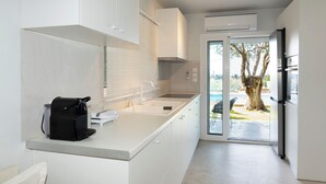 Eine moderne Küche mit weißen Schränken, einem eingebauten Ofen und Blick ins Freie durch eine Glastür.